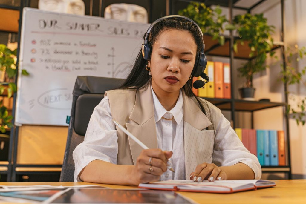 Femme professionnelle portant un casque prenant des notes dans un environnement de bureau, concentrée sur son travail.