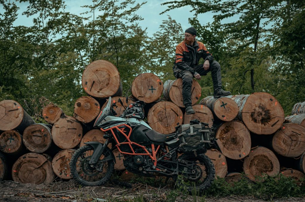 un homme assis sur un tas de bûches à côté d'une moto